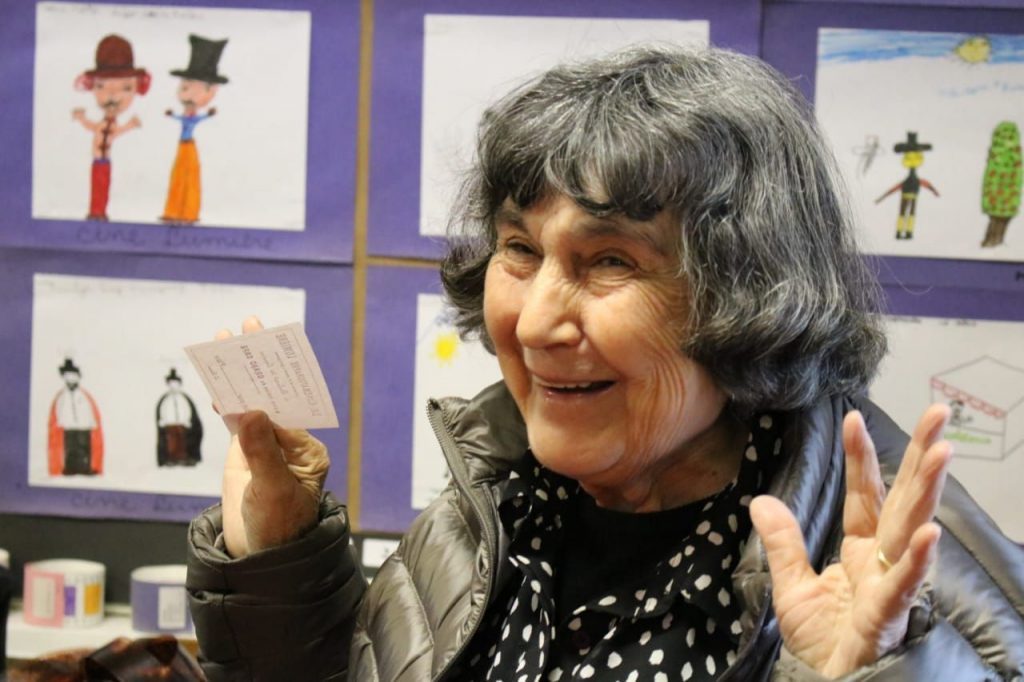 Exposición de Alicia Vega en el GAM: Cine para aprender y jugar Alicia Vega gesticulando durante presentación, con muestra de materiales educativos de cine infantil de fondo