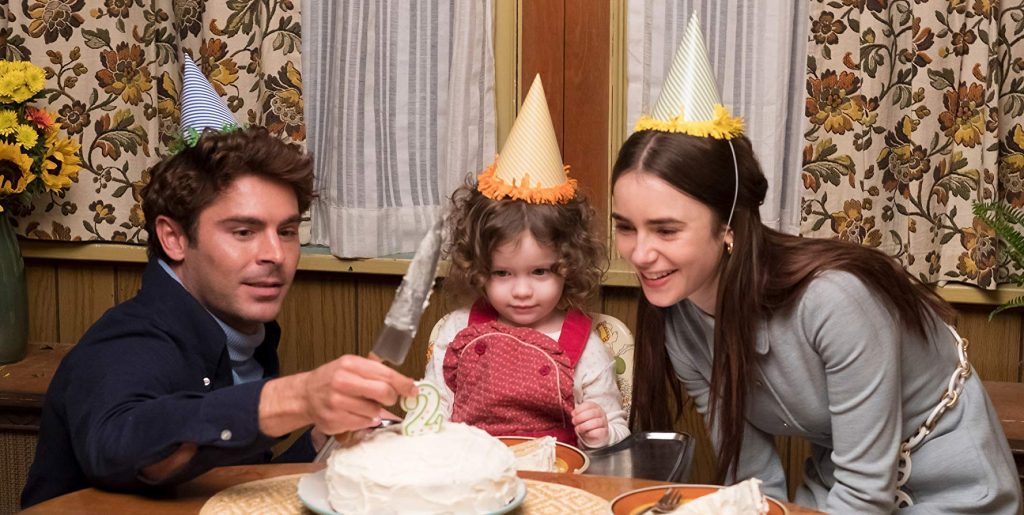 Dos hombres y una niña pequeña en mesa de comedor con papel pintado floral de fondo, escena íntima familiar