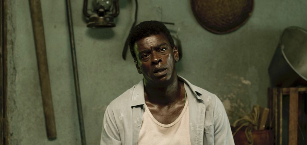 SANFIC 15: "Marighella", de Wagner Moura: Los mecanismos de la efectividad Hombre con gafas y camisa blanca en interior con objetos colgados, escena de la película Marighella