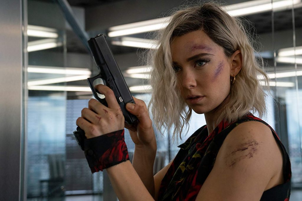 Mujer rubia con pistola en mano dentro de un edificio moderno, lista para combate