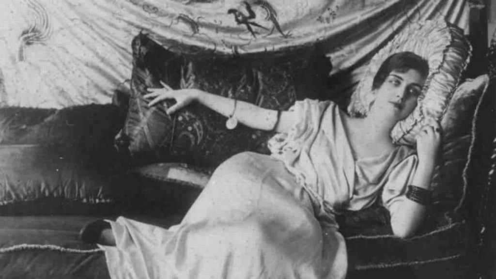 “La mirada”, de Noemí Carrasco: Allí donde las palabras golpean la costa Mujer acostada en cama leyendo un libro, fotografía en blanco y negro de época, ambiente íntimo y literario