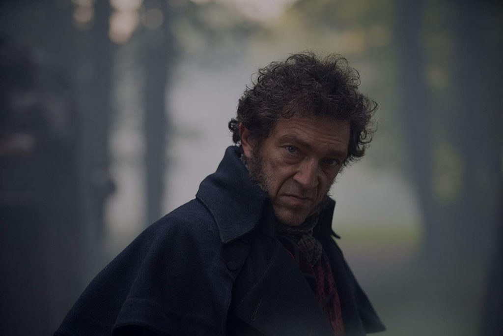 Hombre de mediana edad con cabello rizado, abrigo oscuro, expresión seria bajo lluvia y niebla en ambiente urbano