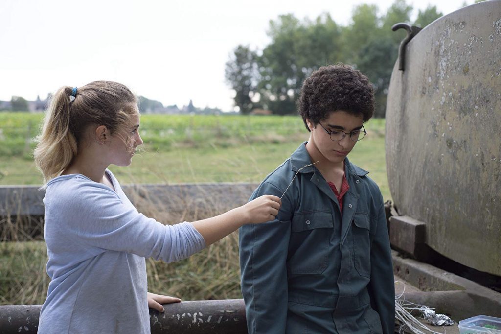 Dos jóvenes junto a un tanque de agua en un campo rural; el muchacho vira la cabeza mientras la chica lo toca