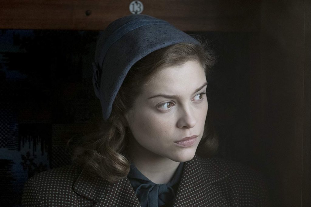 Mujer joven con boina azul y abrigo de lana, mirada seria hacia un lado, iluminación cinematográfica de época