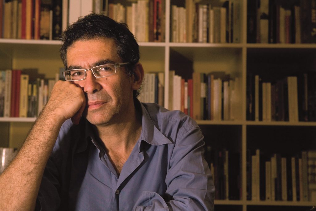 Roberto Brodsky: "En Chile caminamos de lado, mimetizados con la geografía que nos tapa la boca" Retrato de Roberto Brodsky, escritor y crítico cultural, con gafas frente a una estantería de libros