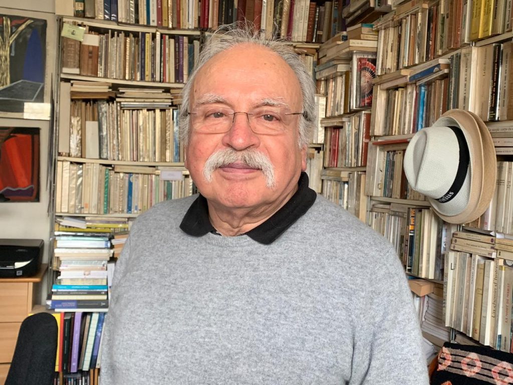 Waldo Rojas, poeta chileno, en su biblioteca rodeado de libros, con gafas y bigote