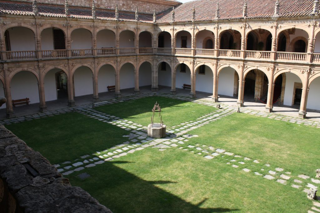 Claustro del Colegio Fonseca con arcadas de piedra, jardín central con césped y senderos de baldosas blancas