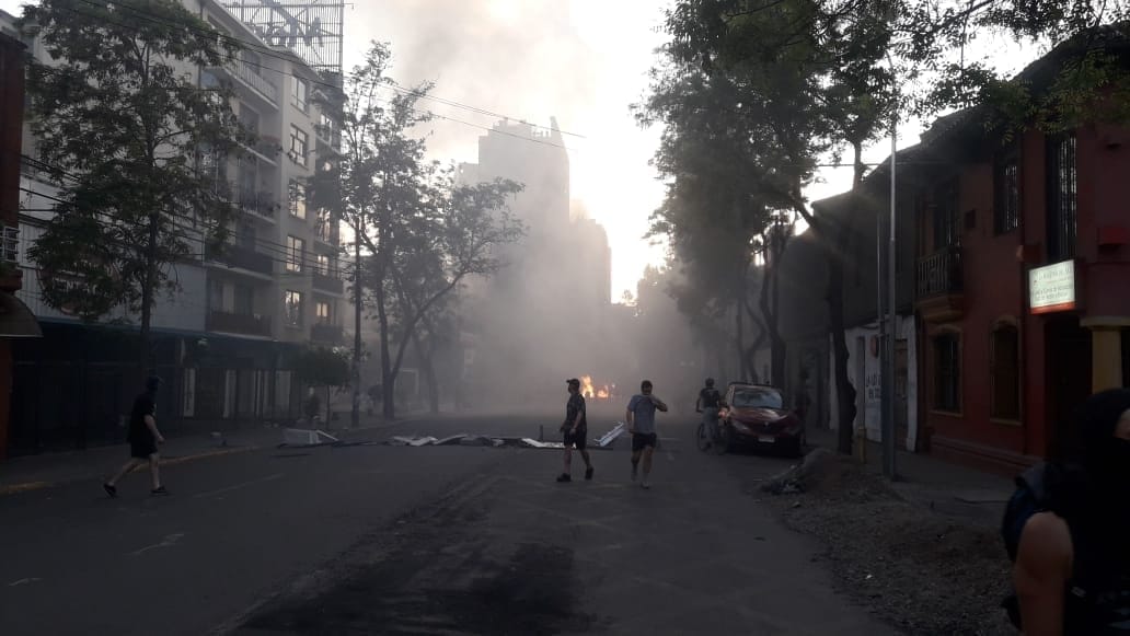Calle urbana envuelta en niebla con edificios de varios pisos, personas caminando y vehículos, atmósfera de crisis