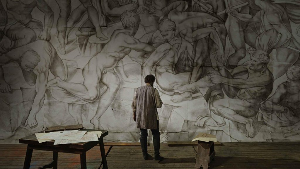 "Michelangelo - Infinito": Revisitando al genio Hombre de pie frente a mural con figuras clásicas dibujadas, ambiente de estudio artístico renacentista
