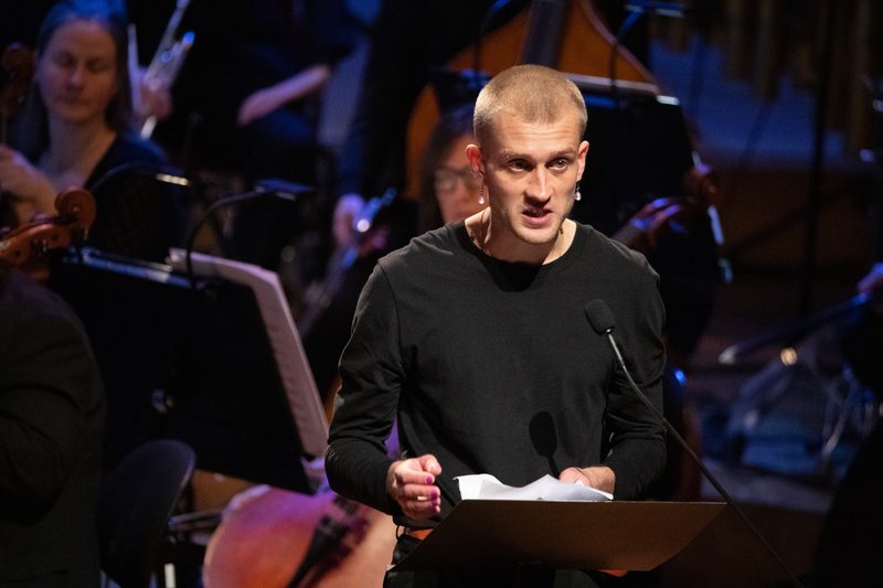 Jonas Eika, escritor danés, en podio durante presentación pública con orquesta de fondo