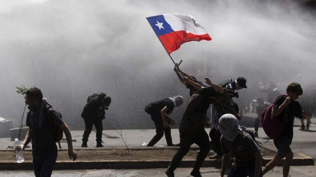Manifestantes sostienen bandera chilena durante protestas callejeras con humo de gases lacrimógenos de fondo