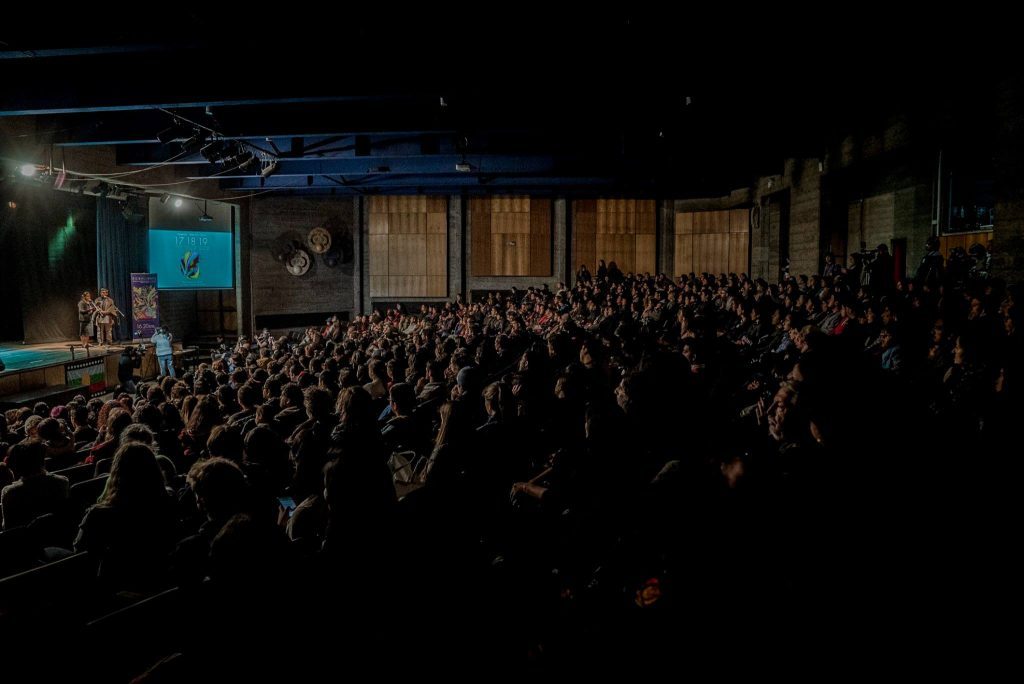 Sala de cine llena de público durante ceremonia de inauguración de festival, escenario iluminado al fondo
