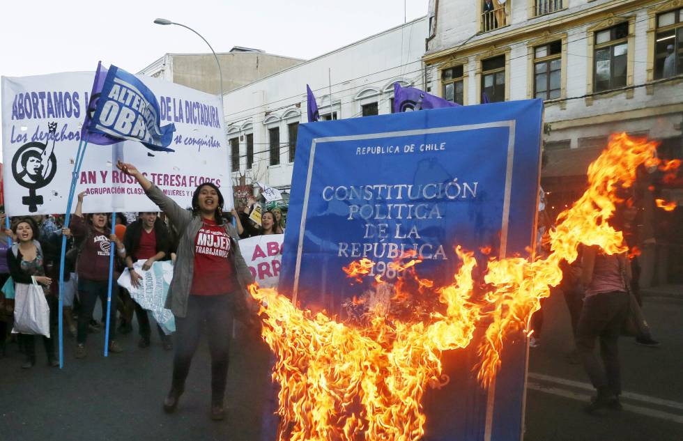 Manifestantes protestan con pancartas y fuego ardiendo frente a documento de Constitución Política en calle