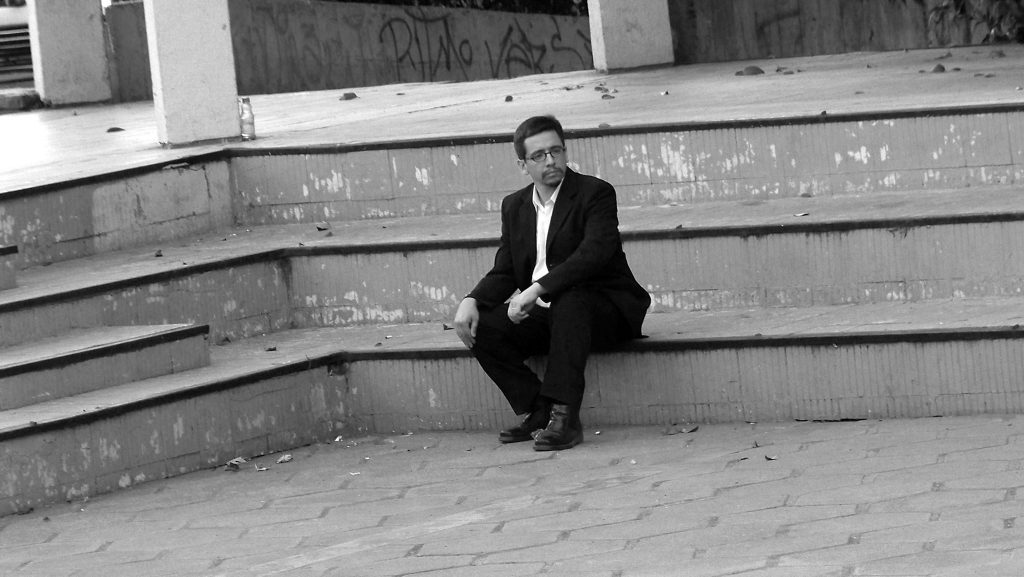 Cristián Arregui Berger sentado en escalones de hormigón, vistiendo traje oscuro, en fotografía blanco y negro