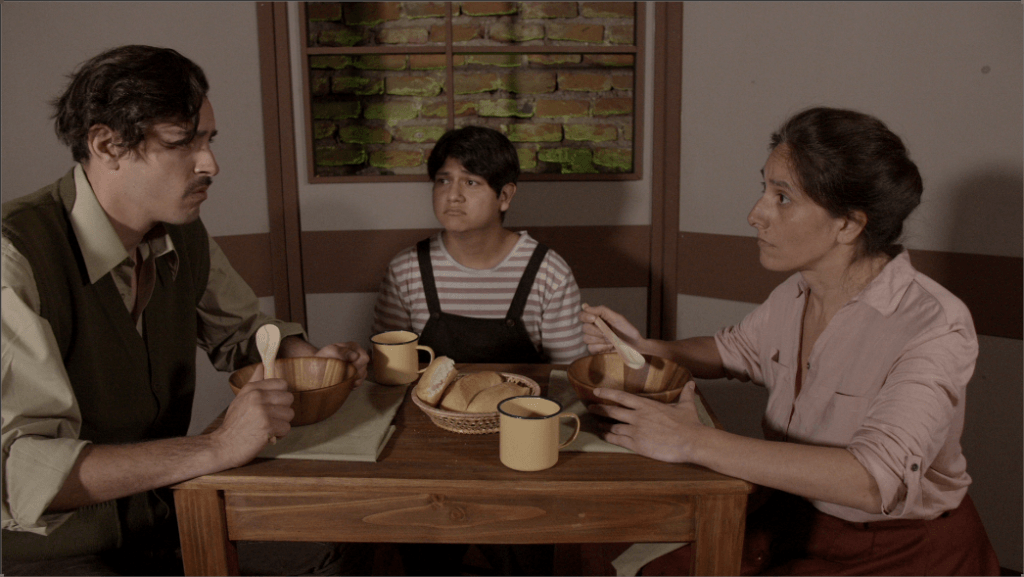 «El reloj de la bestia»: Teatro familiar inclusivo Tres actores en una mesa de madera comparten una escena de teatro, con tazas y platos, en un ambiente de sala interior