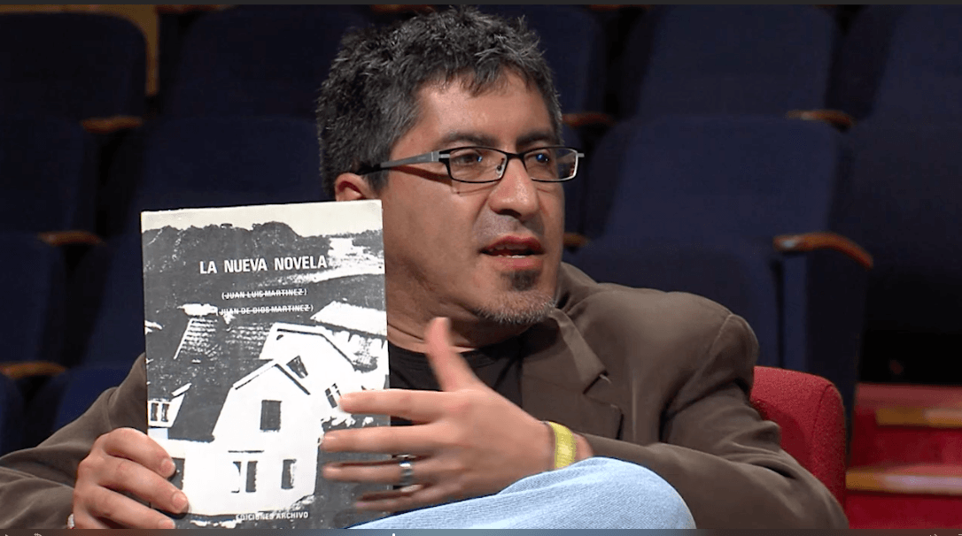 "La vida doméstica", de Marcelo Rioseco: "¿Para qué seguir hablando de la luz, me pregunto, si allá afuera todavía es de noche?" Marcelo Rioseco sostiene un libro durante una entrevista en estudio, vistiendo lentes y chaqueta marrón