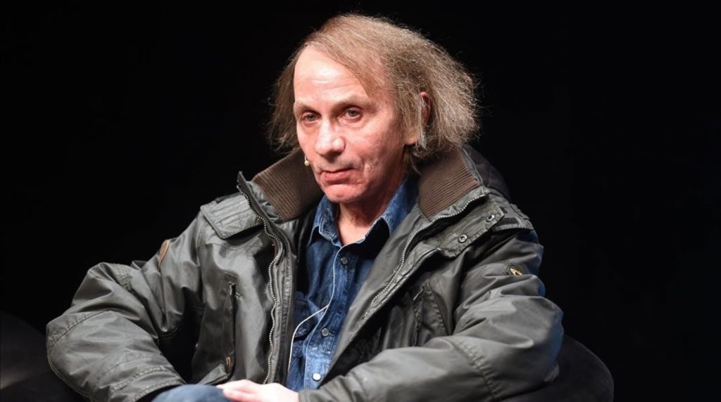 Michel Houellebecq, escritor francés, viste chaqueta gris y camisa azul en primer plano ante fondo negro