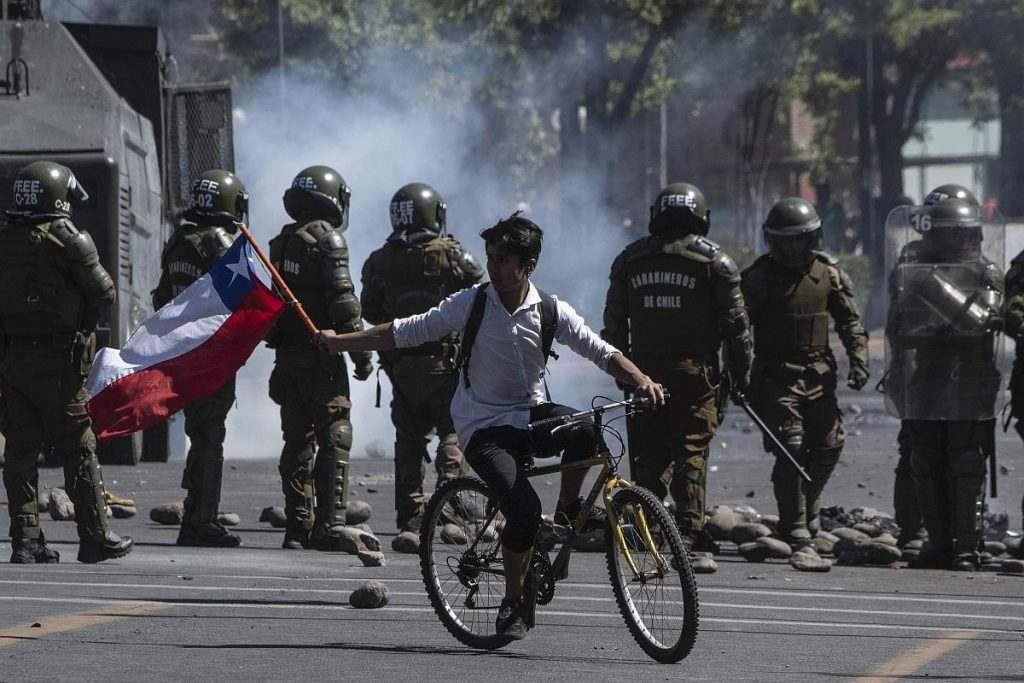 "La clase política o el problema histórico": El Estado es la incertidumbre Manifestantes en calle con policía antidisturbios, humo de gases lacrimógenos, ciclista en medio del enfrentamiento