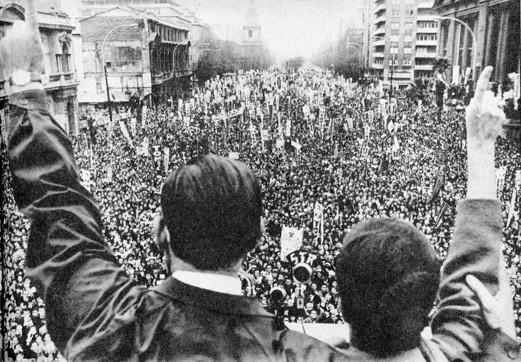 Salvador Allende levanta los brazos ante multitud de manifestantes en plaza pública durante acto político