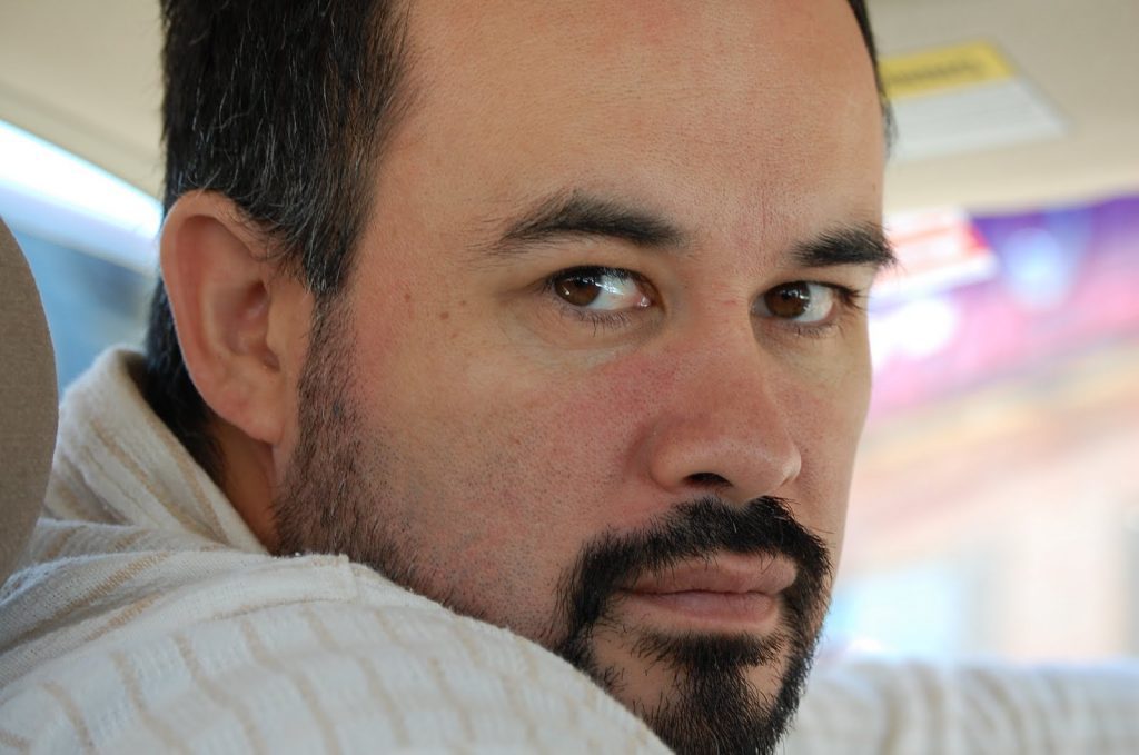 Poeta Cristián Gómez sobre el estallido social: "Es una nueva oportunidad para la política, para la polis, para reinventar lo público y redefinirnos como sujetos sociales" Cristián Gómez, poeta chileno, en primer plano con barba oscura vistiendo camisa clara