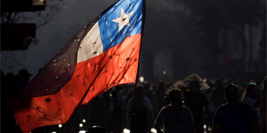 Bandera chilena iluminada durante una manifestación nocturna con multitud de personas de espaldas observando