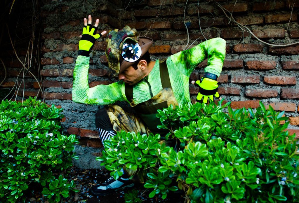 Personaje en traje verde fluorescente saltando entre plantas verdes contra pared de ladrillos rojos en escena de acción