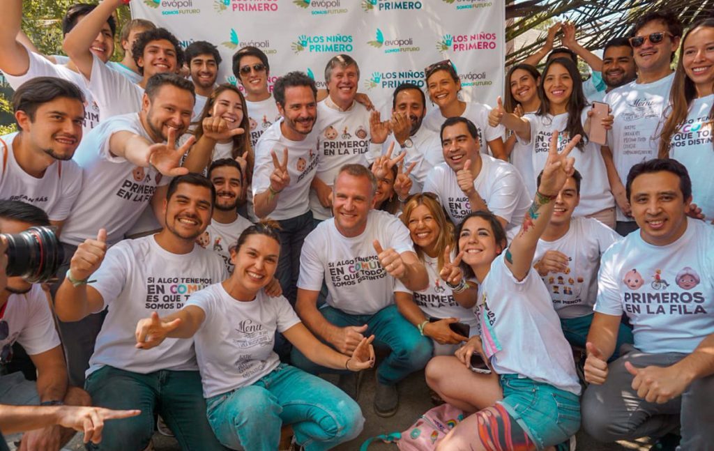 Grupo de personas con camisetas blancas posando frente a panel de logos, evento político o institucional