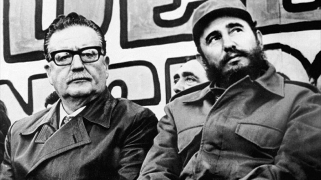 Fidel Castro y otro hombre en uniforme militar conversan en fotografía histórica en blanco y negro