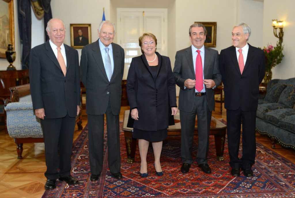 Cinco presidentes de Chile en traje oscuro posando en salón formal con tapete rojo y decoración navideña