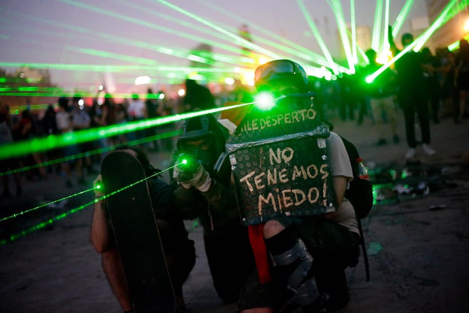 Manifestante sostiene cartel que dice "No tenemos miedo" durante protesta nocturna con luces láser verdes de fondo