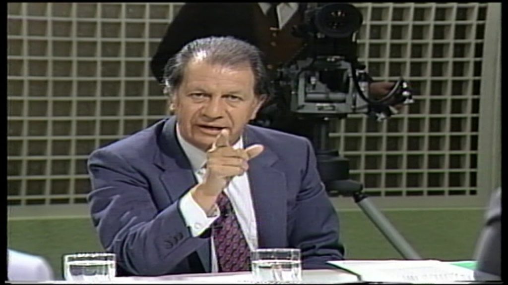 Ricardo Lagos en estudio de televisión, sentado ante micrófono, con gesto pensativo y dedo índice en la boca