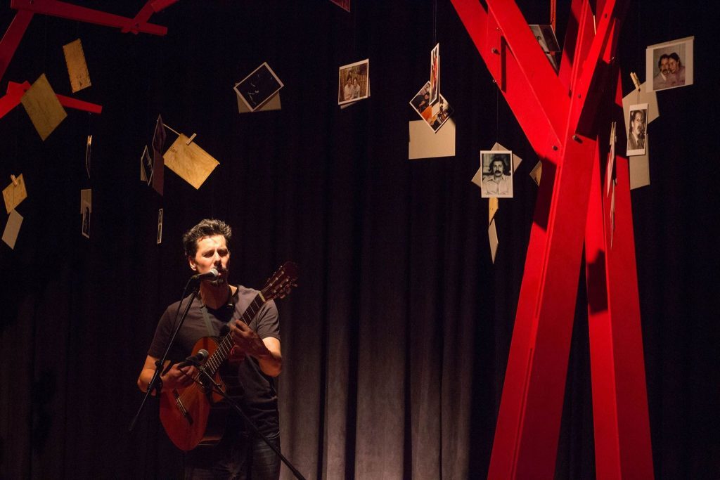 Willy Oddó en escena con violín, rodeado de marcos suspendidos, evocando memoria y exilio artístico
