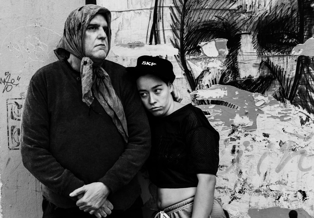 Tres personas en blanco y negro en interior precario, escena de tensión dramática de El Divino Anticristo