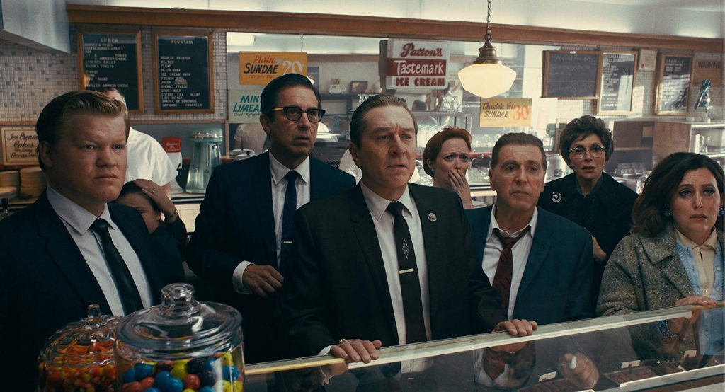 Grupo de hombres en trajes y corbata en un bar, escena de tensión y conversación en ambiente cinematográfico