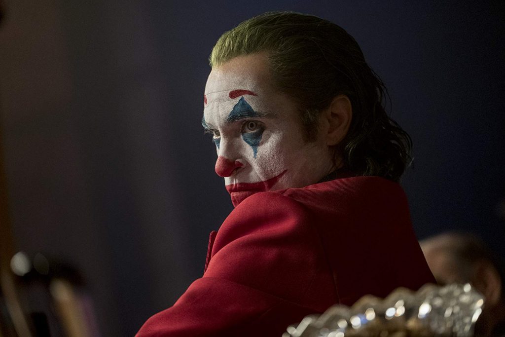 Personaje del Guasón con maquillaje característico y atuendo rojo, mirando hacia un lado en primer plano