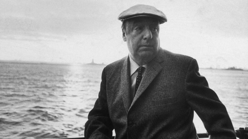 Pablo Neruda con traje oscuro y gorra, junto al mar, en fotografía en blanco y negro