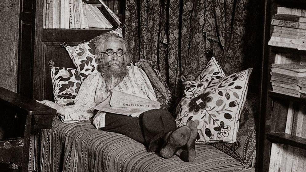 Ramón del Valle-Inclán, escritor español con barba, sentado en un sillón leyendo junto a dos gatos