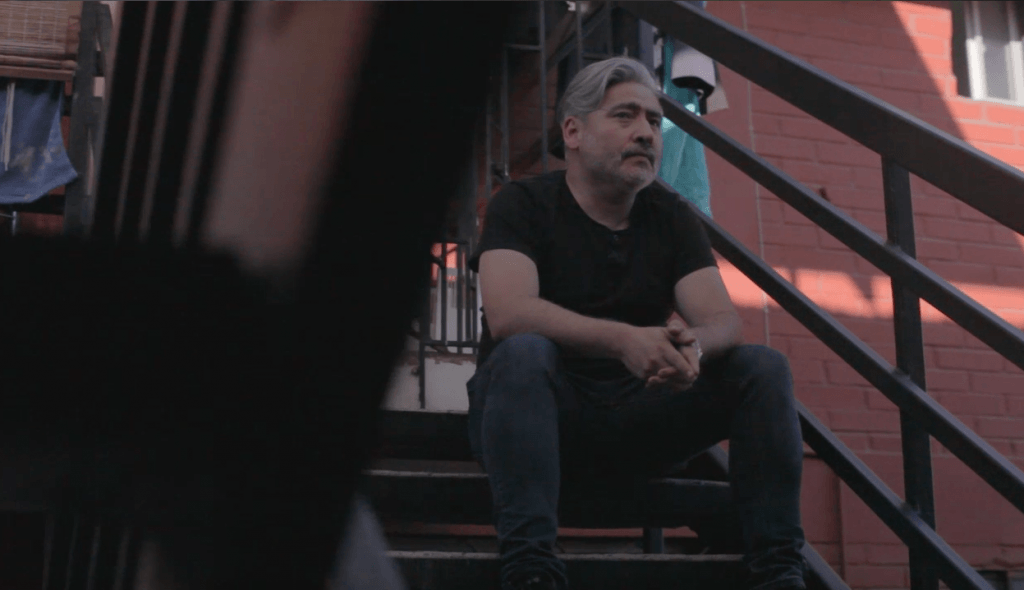 Ernesto Garratt sentado en escaleras de metal, mirando hacia la cámara en ambiente urbano con luz natural