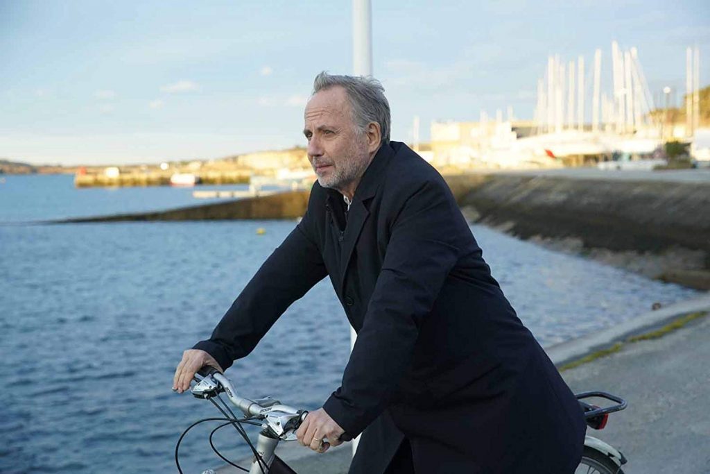 "La biblioteca de los libros olvidados": ¡Desconfiar, desconfiar y después... desconfiar! Hombre mayor en bicicleta junto al mar, con edificios al fondo y luz de atardecer