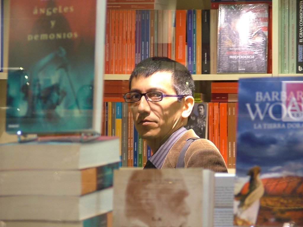 "La muchacha que deseaba vivir en un invernadero", de César Valdebenito: De hecatombes en el Biobío Hombre con lentes en biblioteca, rodeado de libros y carteles de eventos literarios