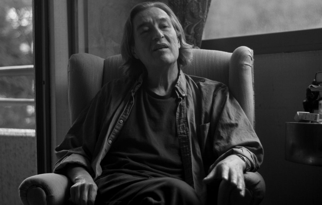 Gonzalo Contreras, escritor chileno, sentado en un sillón con la cabeza reclinada, fotografía en blanco y negro