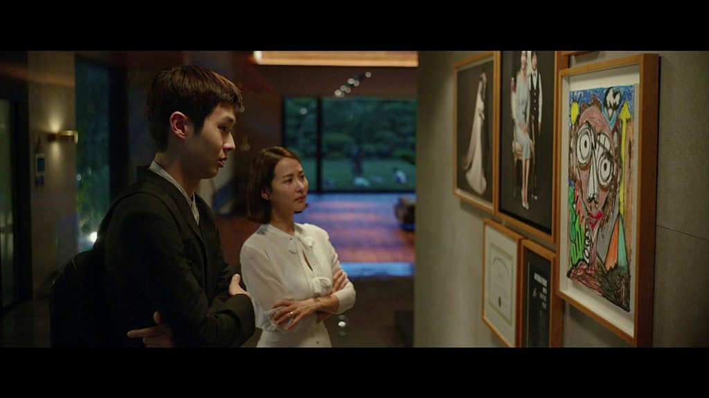 "Parasite": Una idea de "estallido social" cinematográfico Dos hombres observan cuadros en una galería de arte iluminada; uno viste traje oscuro y el otro camiseta blanca