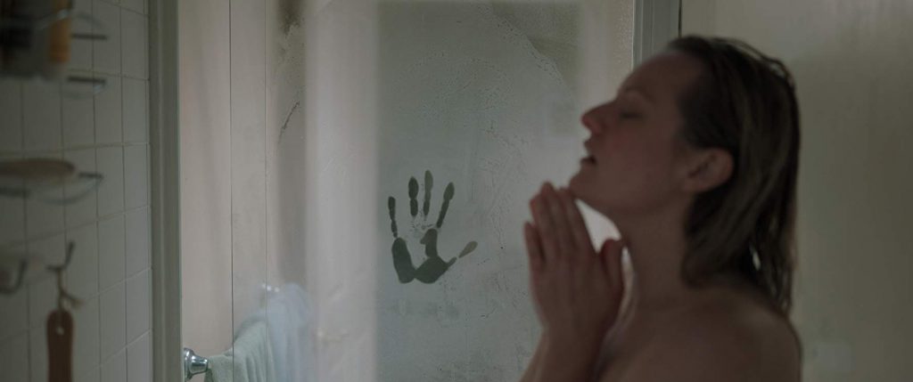 "El hombre invisible": El retrato de una dama vulnerable Mujer en ducha tocándose el rostro con expresión de angustia, mano de hombre visible en el espejo detrás de ella