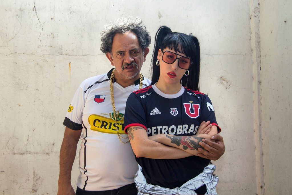 «Cómo cuidar de un pato»: Azul y blanco Dos hombres posan juntos frente a pared blanca; uno viste camiseta deportiva blanca y amarilla, el otro camiseta negra