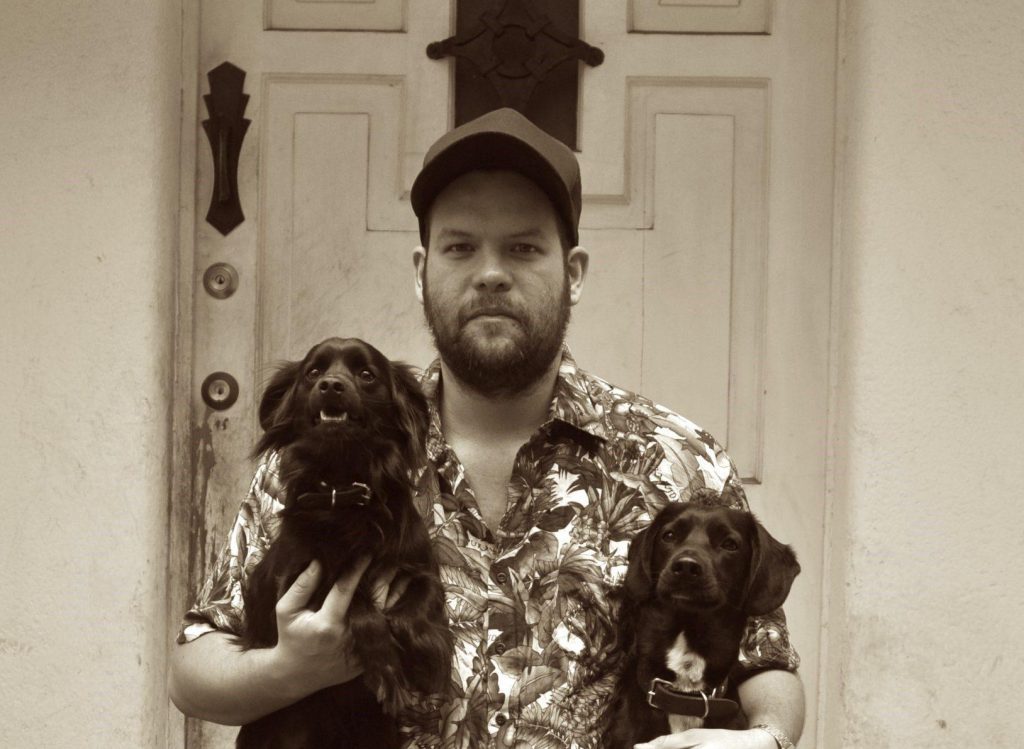 Hombre con gorra y camisa floral sosteniendo dos perros de raza cocker spaniel de color marrón en sus brazos