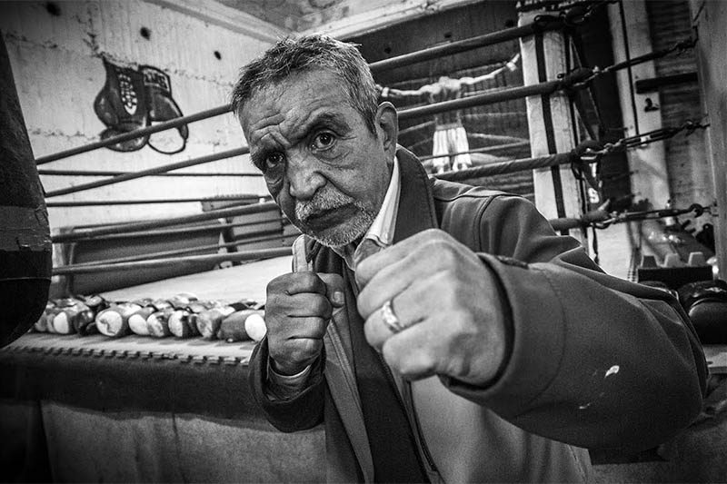 Subestimar al enemigo: Evópoli y su plan de “depuración cultural” Hombre mayor en posición de boxeo defensiva dentro de un estudio o gimnasio, fotografía en blanco y negro