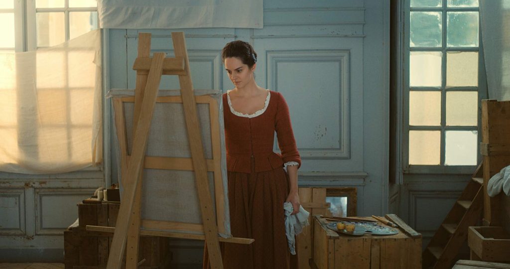Mujer en vestido marrón junto a un lienzo en taller de pintura, luz natural atraviesa ventanas de fondo