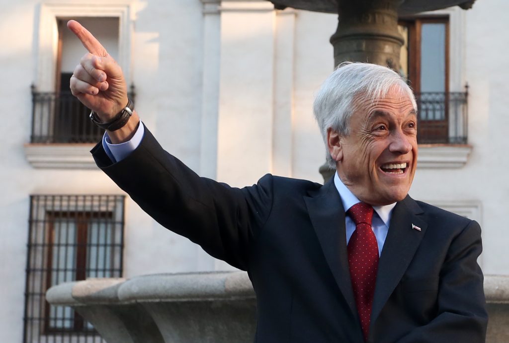 "La importancia de llamarse Sebastián": Una destitución imposible Sebastián Piñera levanta el puño en gesto de victoria frente a edificio colonial, vistiendo traje oscuro y corbata roja