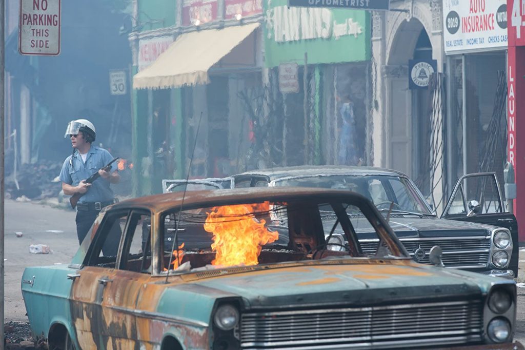 Cine de mundos en peligro: "Detroit: Zona de conflicto", días extraños en el imperio Auto abandonado en llamas en una calle urbana deteriorada, con edificios comerciales de fondo y figura en la acera