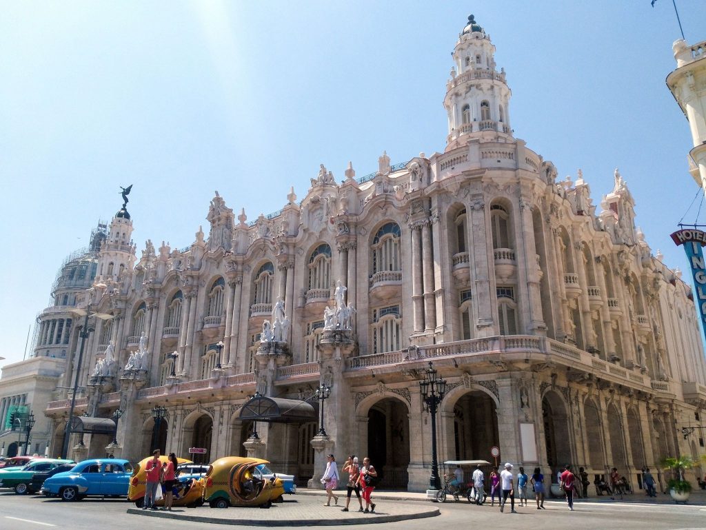Gran Teatro de La Habana con fachada ornamentada de estilo Beaux-Arts, automóviles clásicos y transeúntes en la plaza